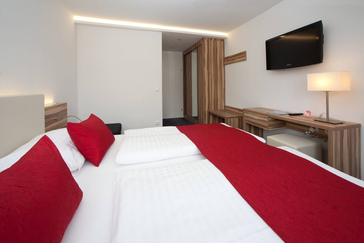 A hotel room with a bed, a desk, a chair, a TV, and a mirror.