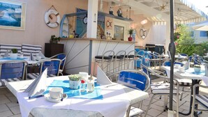 An outdoor café with striped tables and chairs, a bar area, and nautical-themed decorations. - Happy House das fröhliche Urlaubszuhause (Krumpendorf am Woerther See)