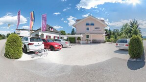 A hotel with a parking lot, several cars, and flags. - Happy House das fröhliche Urlaubszuhause (Krumpendorf am Woerther See)