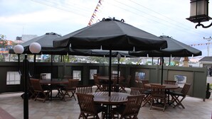 Un patio al aire libre con varias mesas y sillas de madera, cubierto por grandes sombrillas negras.