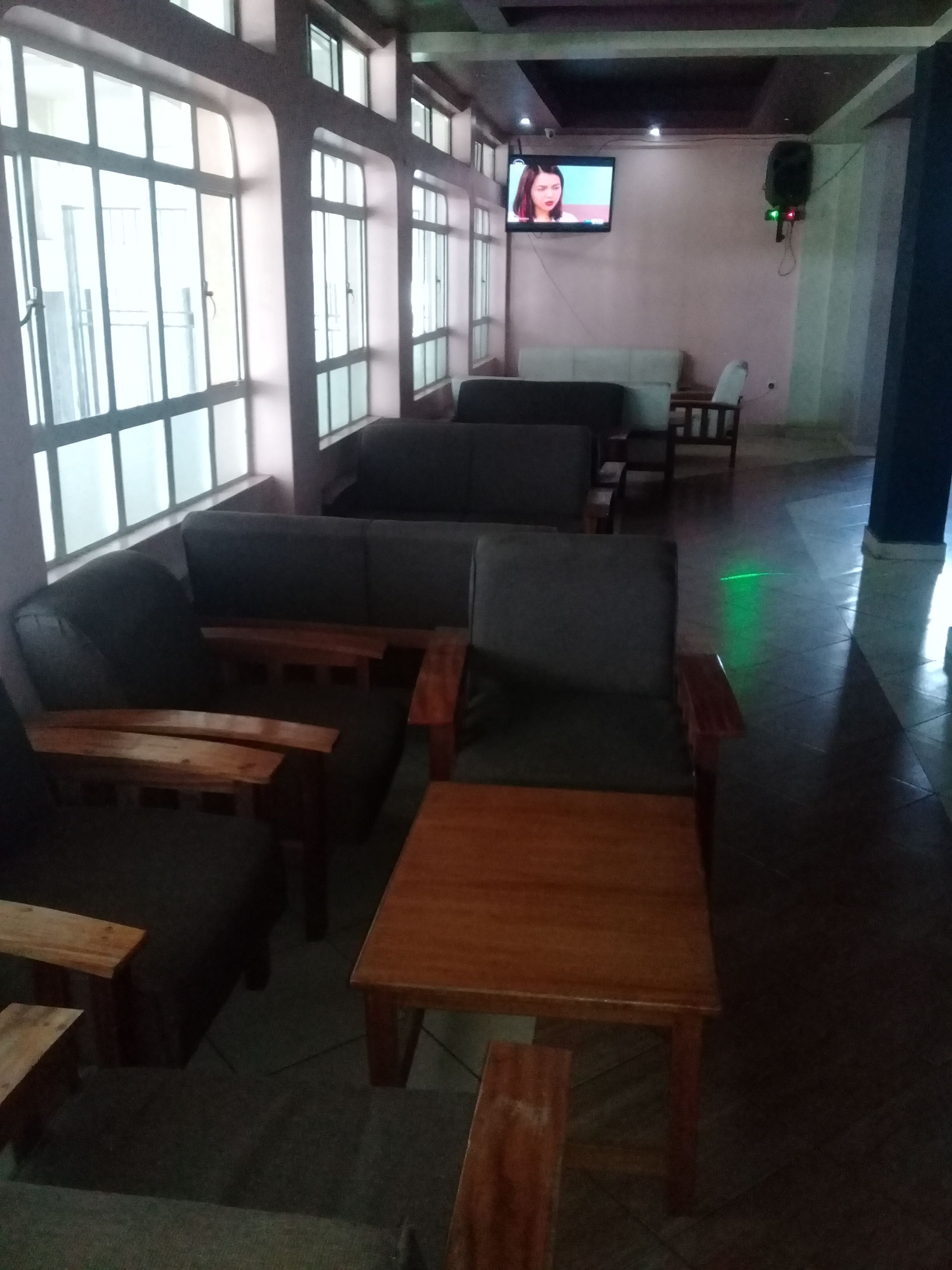 A seating area with sofas and tables, large windows, and a television on the wall.
