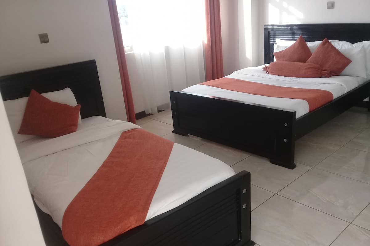 Habitación de hotel con dos camas, cada una con ropa blanca y detalles color naranja.