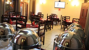Un restaurante con varias mesas y sillas, un televisor en la pared y piso de baldosas.