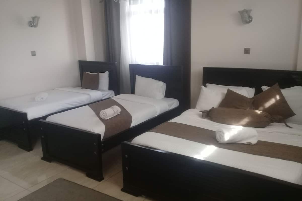 Habitación de hotel con tres camas individuales, cada una con una almohada y una toalla enrollada.