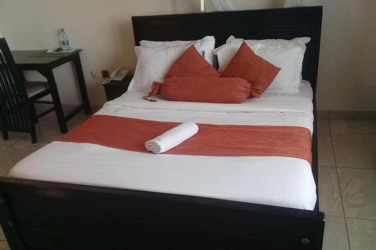Una cama bien tendida con ropa de cama blanca y roja, una toalla enrollada y una mesita de noche con un teléfono y una botella de agua.