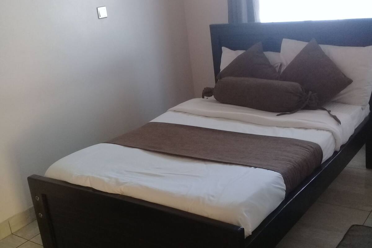 Una cama individual con estructura oscura, ropa de cama blanca y varias almohadas.