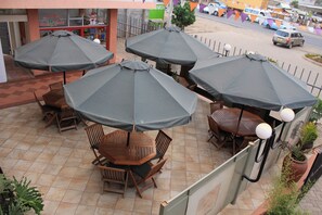 A patio area with multiple wooden tables and chairs, each under a grey umbrella.