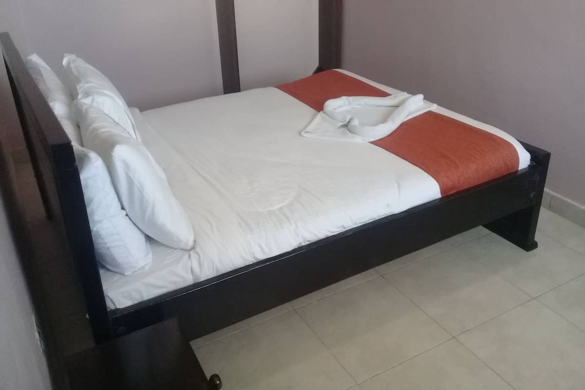 Una cama individual con ropa blanca y un detalle rojo, un cabecero de madera y suelo de baldosas.