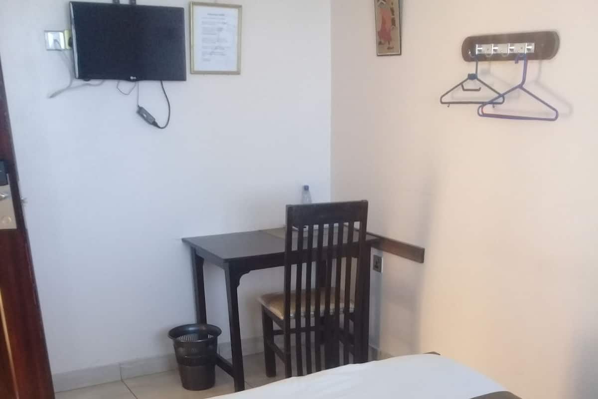 Un dormitorio con cama, escritorio, silla, televisor y perchero en la pared.