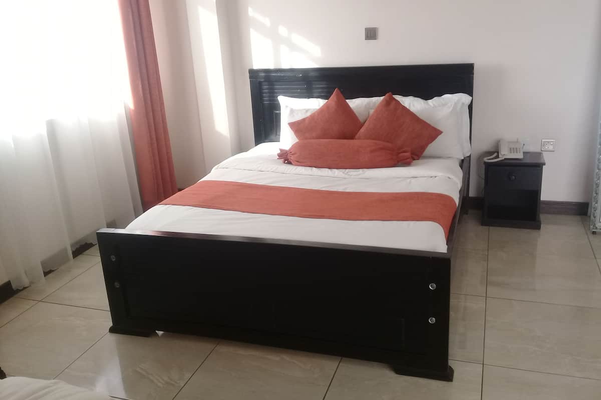 Una cama con estructura negra, ropa de cama blanca y almohadas naranjas. Hay una mesita de noche con un teléfono y un enchufe.