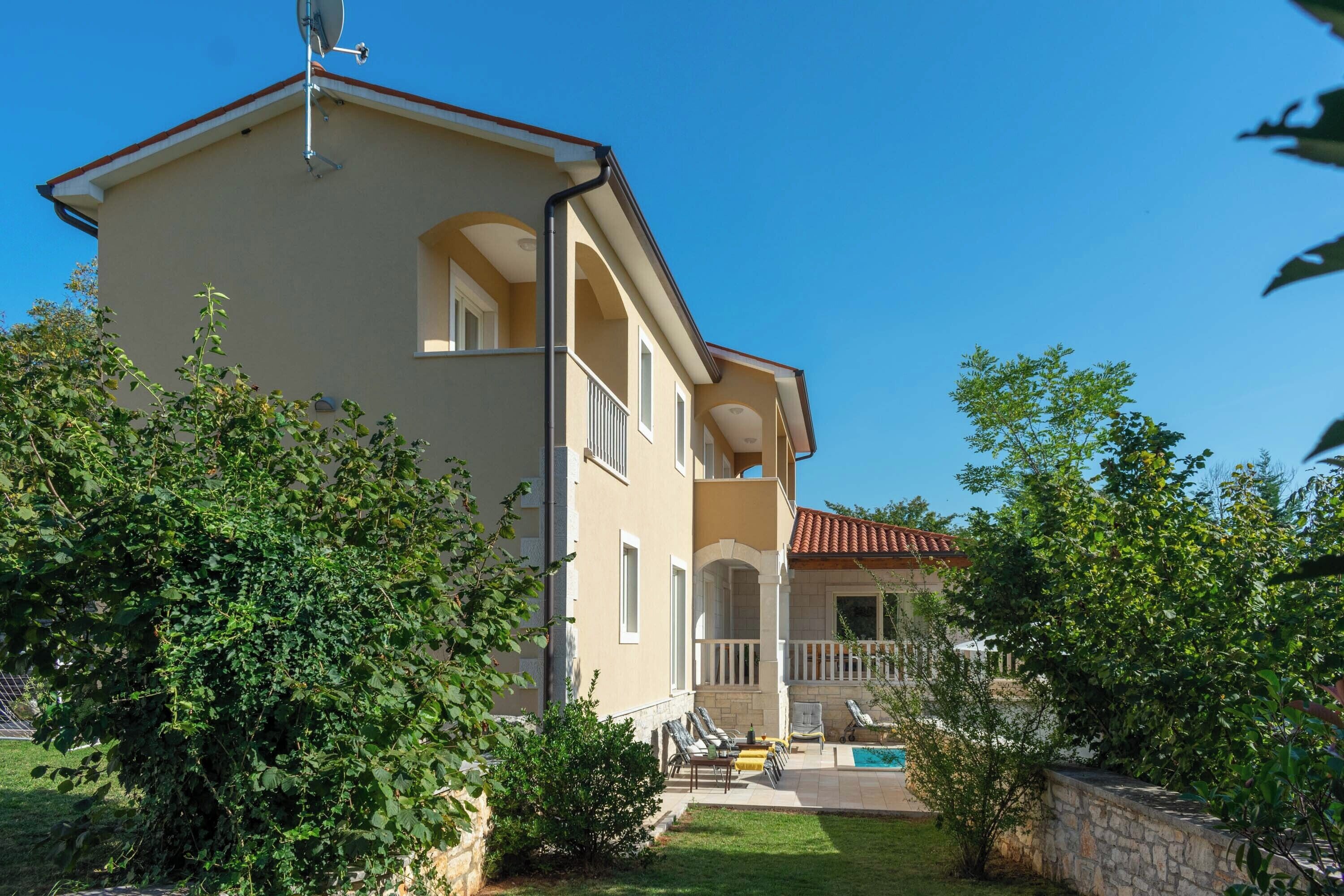 A two-story building with a balcony, a swimming pool, and a stone wall.