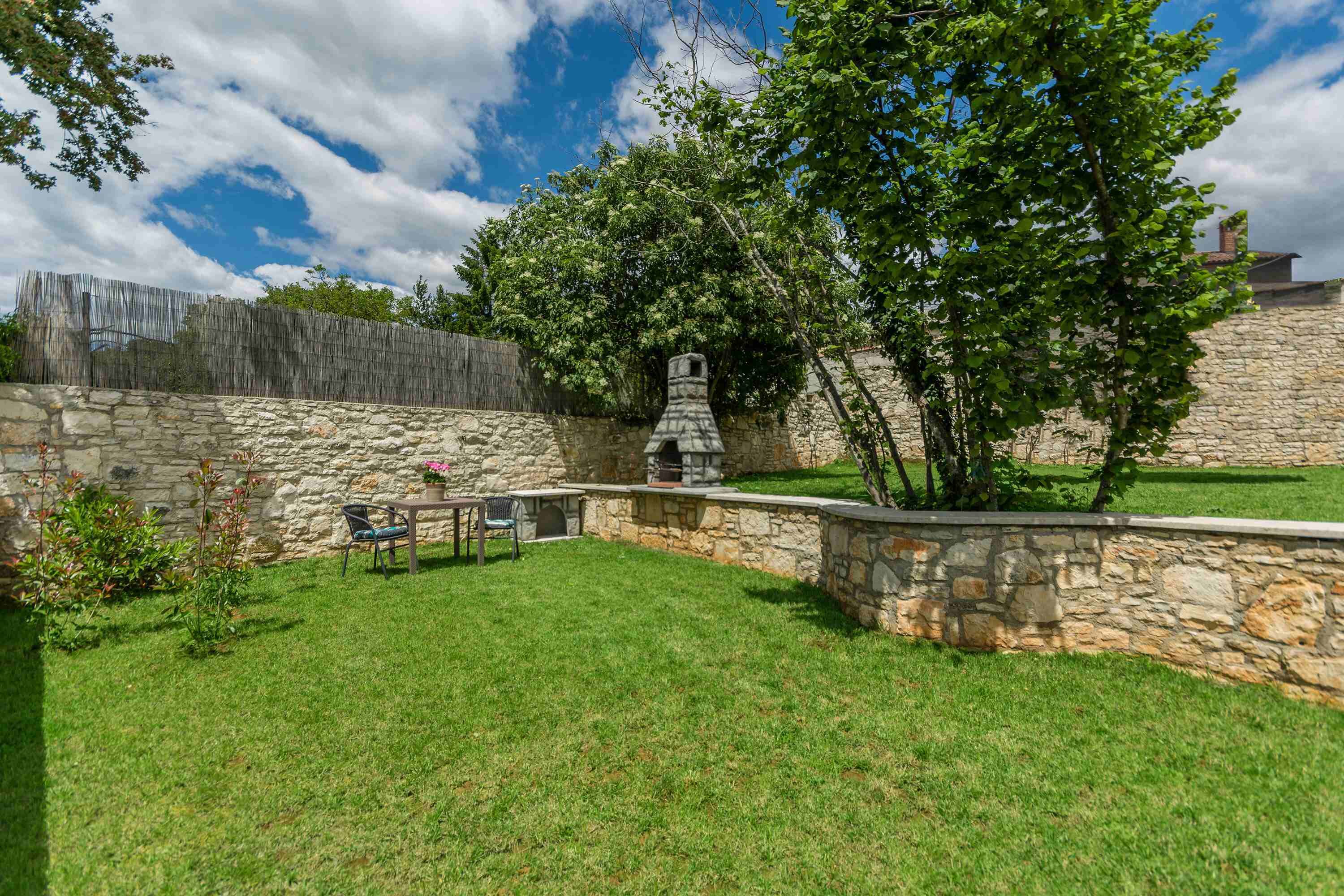 Un patio trasero con muro de piedra, cerca de madera y zona de parrilla.