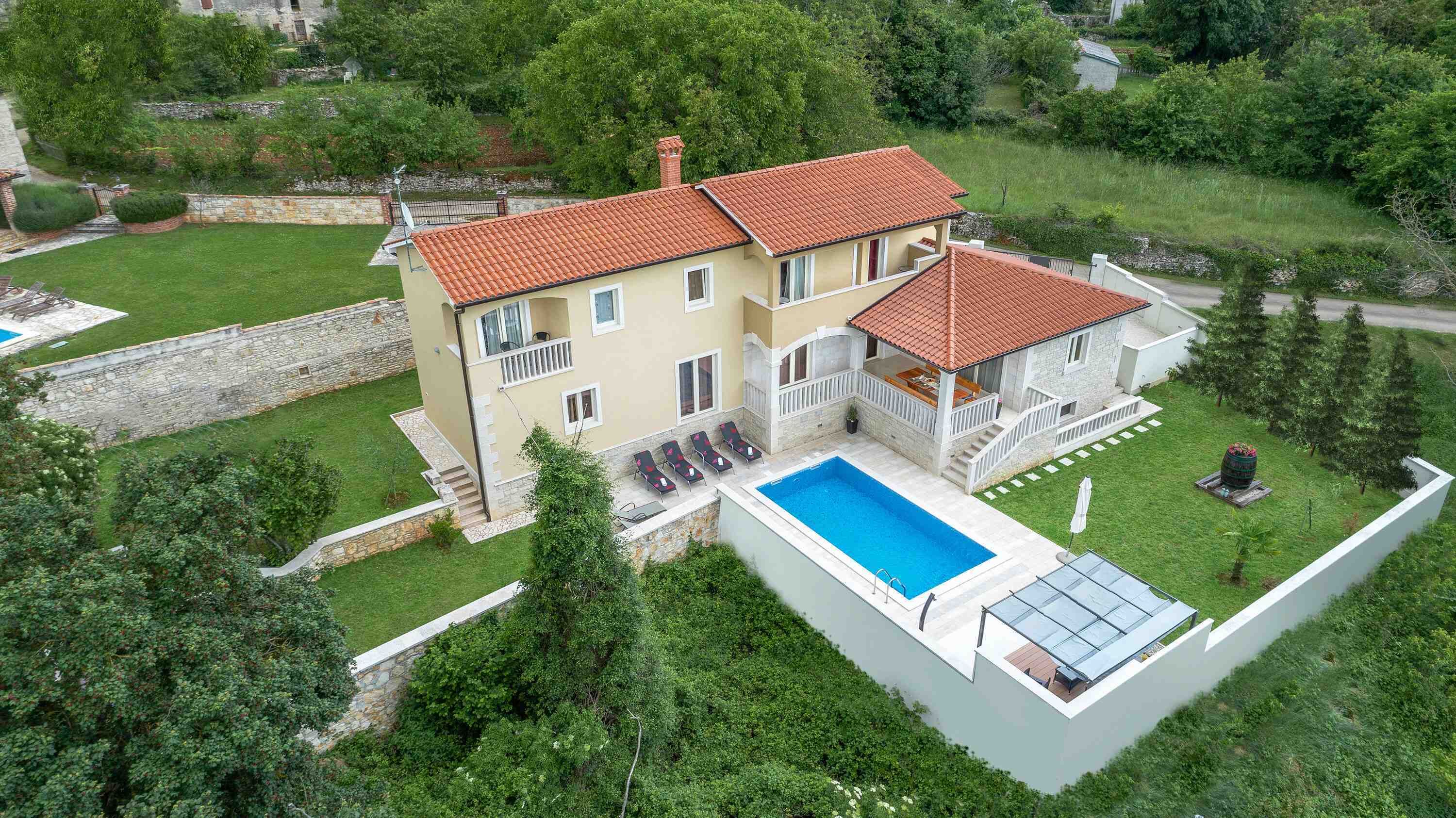 A two-story house with a swimming pool, a covered patio, and a stone wall.
