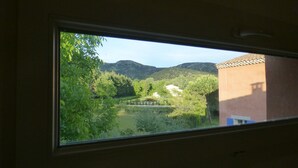 A window view of a mountainous landscape with trees and a building. - Charming contemporary gîte: wooded property, private pool, Luberon view (Cavaillon)