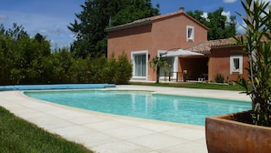 A swimming pool with a tiled deck, a patio area with outdoor furniture, and a building with a red facade and white trim. - Charming contemporary gîte: wooded property, private pool, Luberon view (Cavaillon)