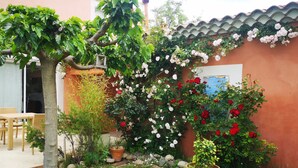 A garden with a variety of plants, a patio with wicker furniture, and a building with a tiled roof. - Charming contemporary gîte: wooded property, private pool, Luberon view (Cavaillon)