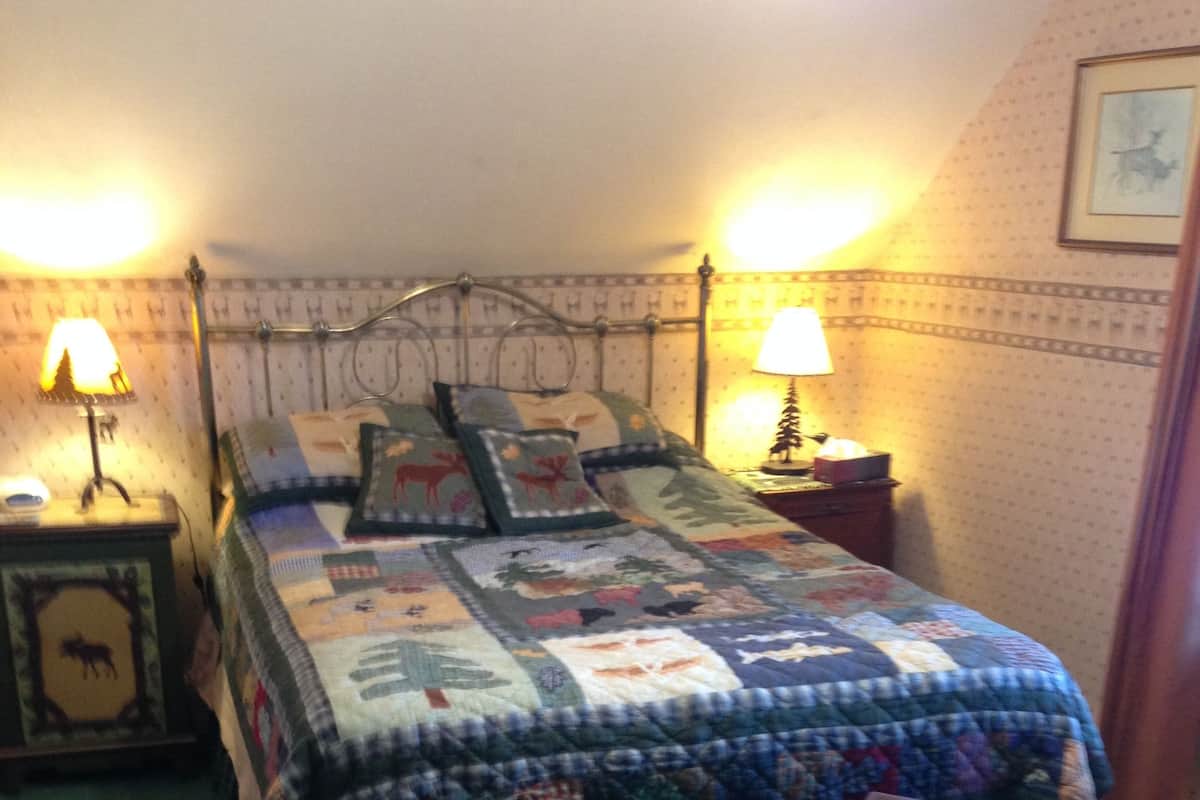 A neatly made bed with a quilt, two bedside lamps, a framed picture on the nightstand, and a small round table with a lamp.