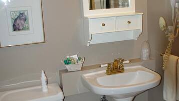 A bathroom with a toilet, sink, and mirror. There is a trash can and a framed picture on the wall.
