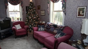 A living room with a pink sofa, a red armchair, a television, and a Christmas tree. - Angel House B&B (Clearview)