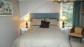 A bedroom with a large bed, two bedside lamps, a chair, and a window with curtains. - Angel House B&B (Clearview)