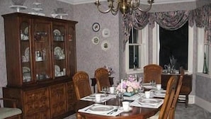 A dining room with a wooden table set for four, surrounded by chairs. A large wooden cabinet with glass doors is to the left. - Angel House B&B (Clearview)