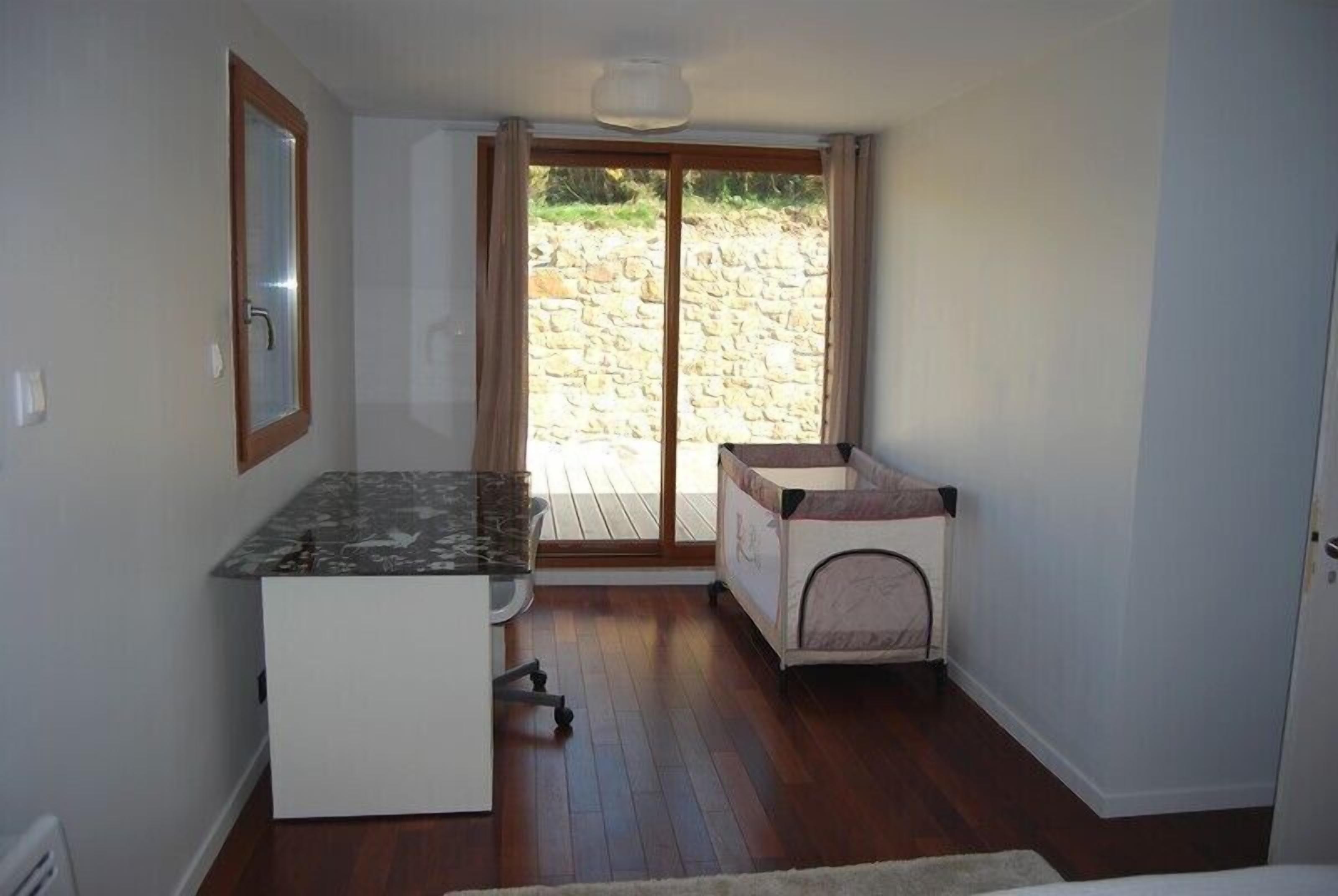 Habitació senzilla amb una cuineta petita, una porta corredissa de vidre que dona a una zona exterior i un parc infantil.