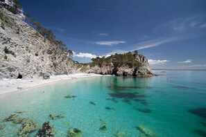 Een kuststrand met helder turquoise water, rotsachtige kliffen en een klein eiland.