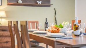 Una mesa de comedor dispuesta con platos, vasos y una botella de vino. Sillas colocadas alrededor de la mesa.