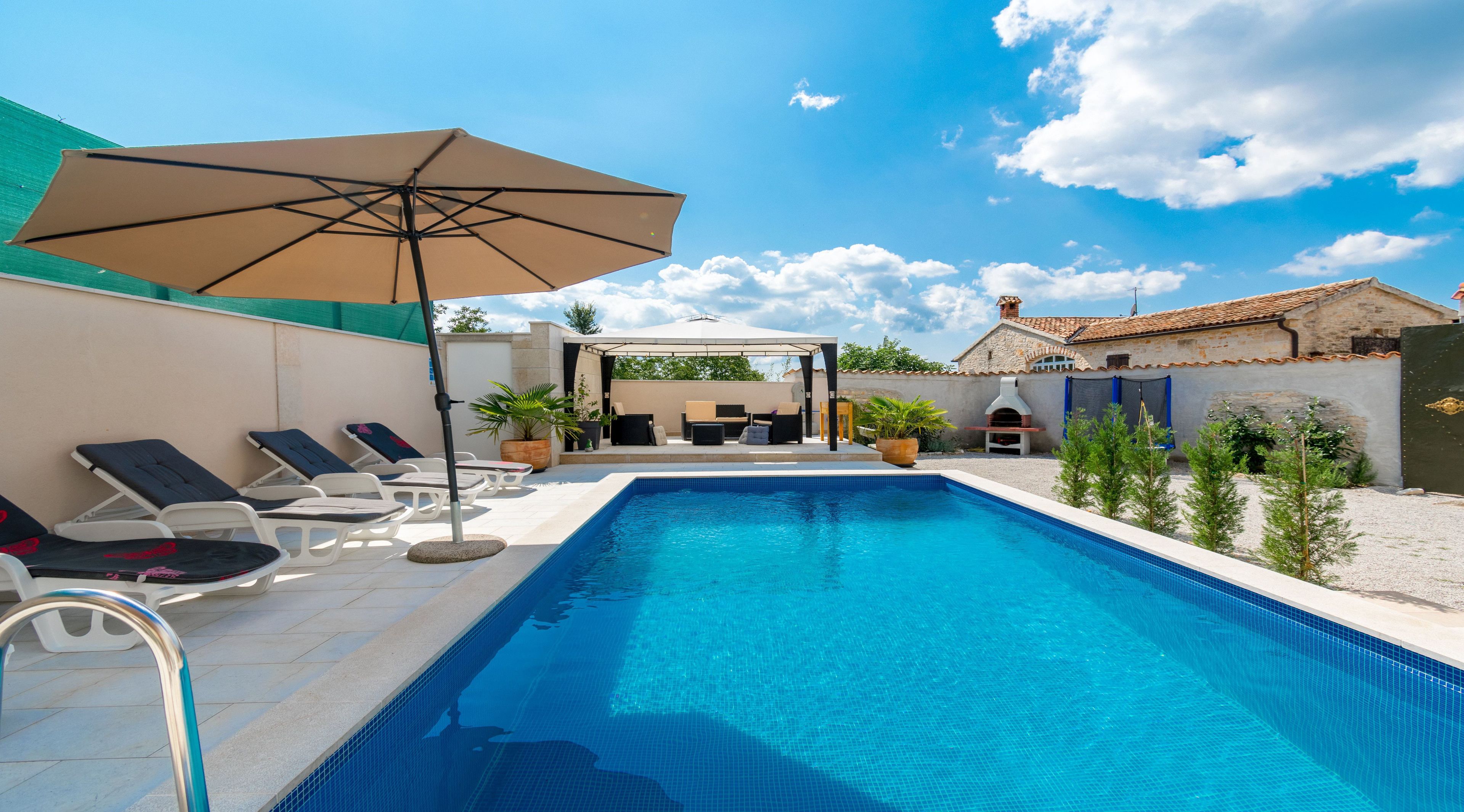 A swimming pool with lounge chairs and a covered seating area.