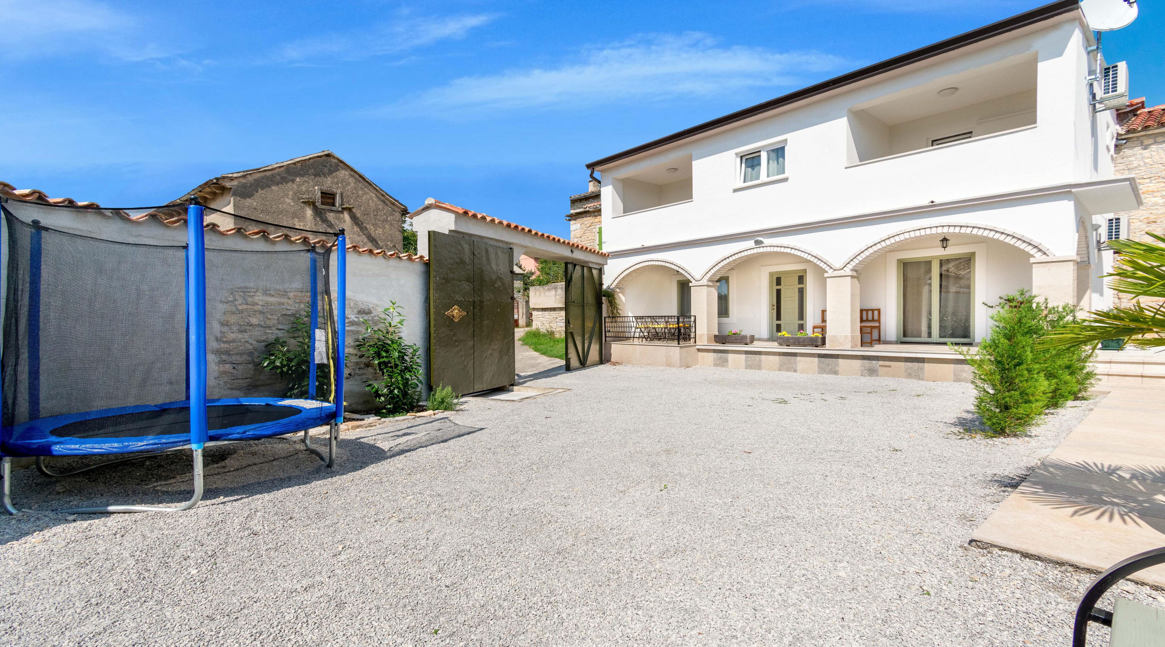 A courtyard with a trampoline, a gated entrance, and a building with arched doorways and a tiled roof.