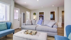 A spacious living room with a grey sectional sofa, a blue armchair, and a white ottoman.