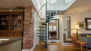 Ein geräumiger Wohnbereich mit Kamin aus Ziegelsteinen, einer Wendeltreppe und einem Essbereich im Hintergrund.