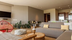 A modern living room with a grey sofa, red chair, and a flat-screen TV mounted on the wall.