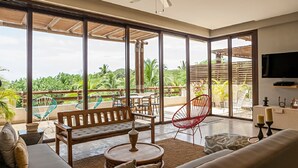 A spacious living room with a large sliding glass door leading to a balcony, a ceiling fan, and a flat-screen TV mounted on the wall.