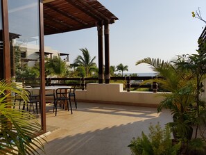 A terrace with a table and chairs, palm trees, and a view of the sea.