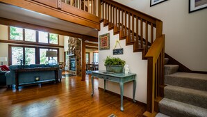 A spacious living area with a wooden staircase, a stone fireplace, and a dining area with a view of the outdoors. - Blue Water Retreat - Spacious Lake Michigan retreat with In-ground pool (Benton Harbor)
