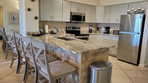 Una cocina moderna con una isla central, electrodomésticos de acero inoxidable y taburetes de bar.
