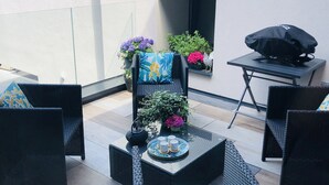 Uma área de pátio com móveis de vime, uma mesa com uma bandeja de chávenas e plantas em vasos.