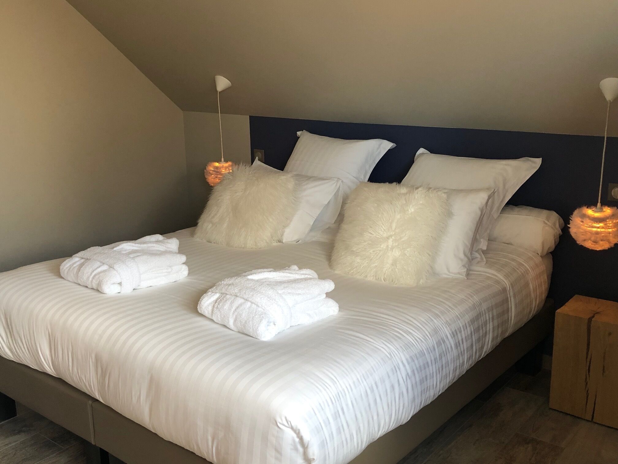 A neatly made bed with white linens, fluffy pillows, and two white towels folded at the foot of the bed.