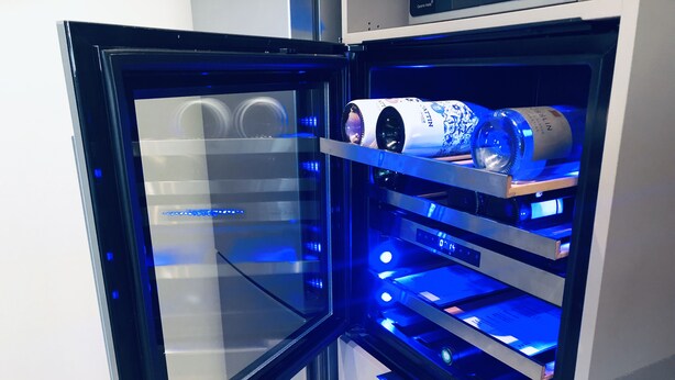 Geladeira aberta com luz interna azul, contendo uma garrafa e um recipiente.