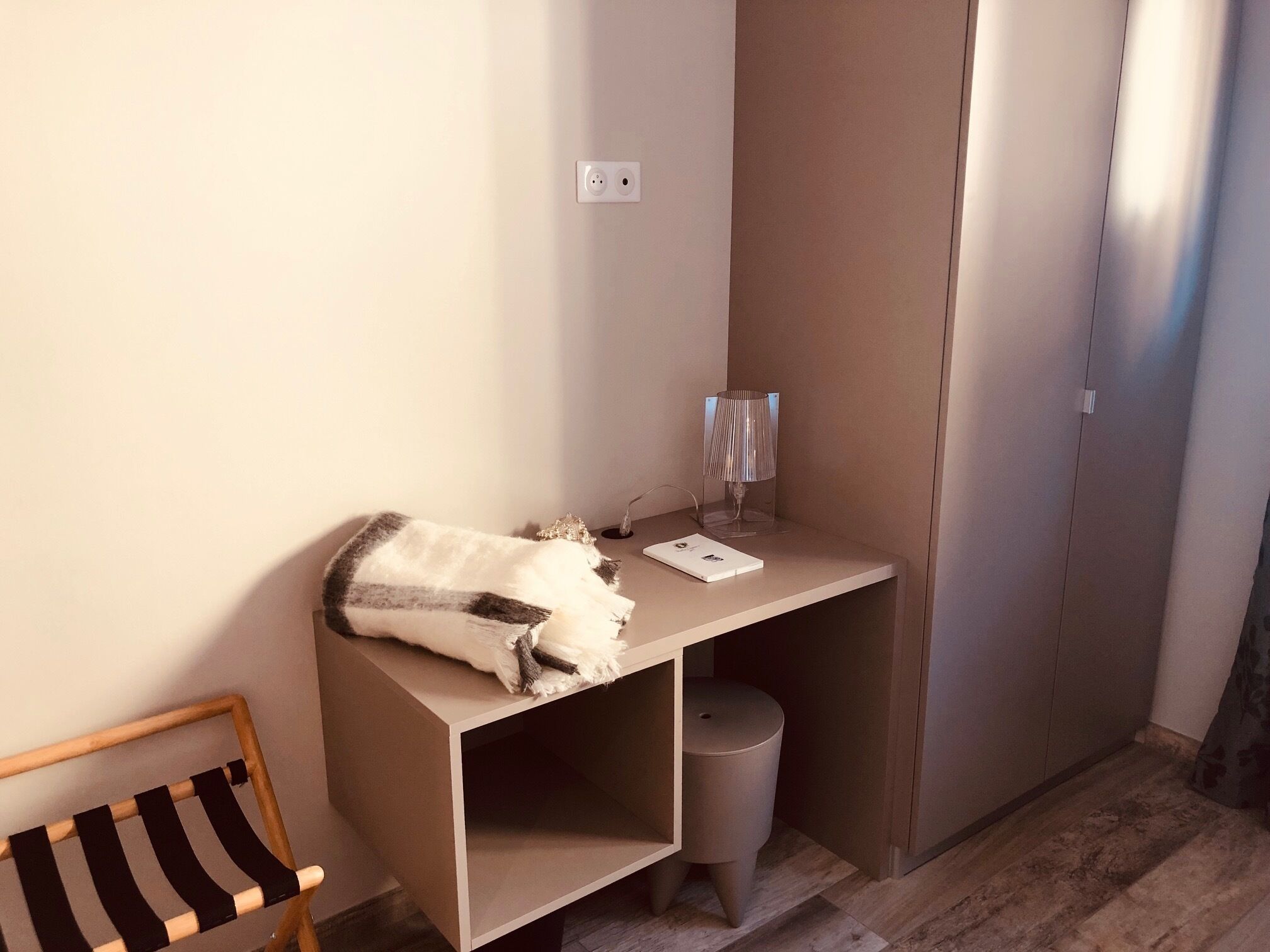 A small, compact room with a desk, a chair, a lamp, and a trash bin.