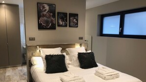 Quarto moderno com uma cama grande, roupa de cama branca e almofadas decorativas pretas. Três obras de arte emolduradas estão penduradas na parede acima da cama.