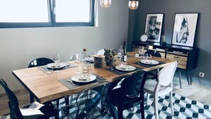 Uma sala de jantar com mesa de madeira posta para quatro pessoas, cadeiras pretas e iluminação pendente.