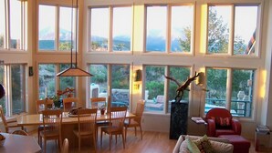 A spacious living room with large windows, a dining area, and a red armchair.