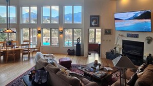 A spacious living room with large windows, a fireplace, and a flat-screen TV.