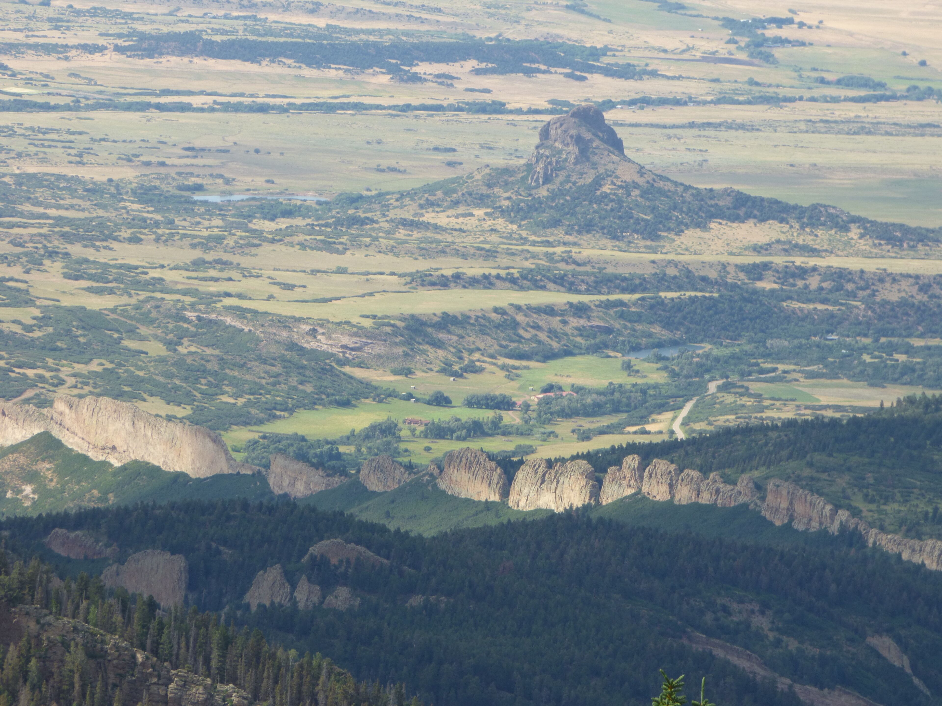 Un paisaje montañoso con un pico rocoso destacado y zonas boscosas.