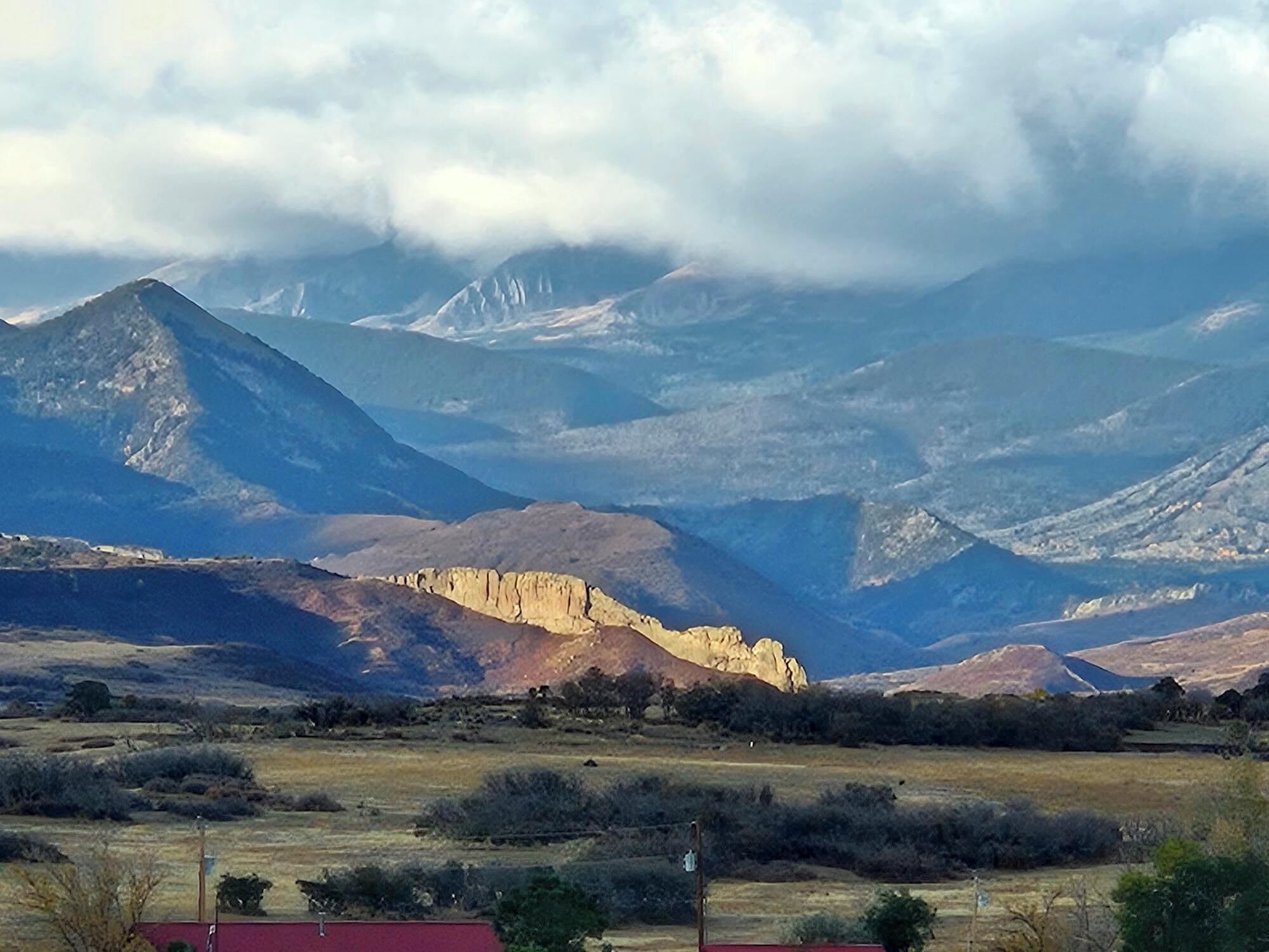 A mountainous landscape with a prominent rocky outcrop in the foreground and a range of mountains in the background.
