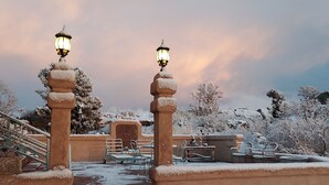 A snow-covered outdoor area with steps leading to a building entrance, two lantern-style lights, and a bench.
