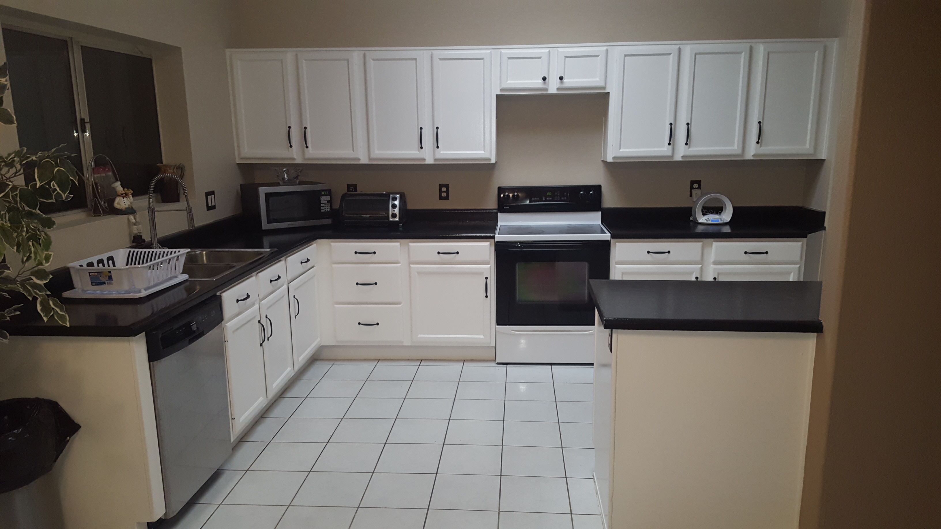 A kitchen with white cabinets, a black countertop, a microwave, a toaster, and a stove.