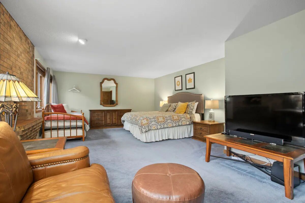 A bedroom with a bed, a TV, a wooden bench, a leather armchair, and a hanging coat rack.